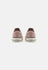 Baskets Converse All Star en daim rose avec un design basse, des rayures noires sur la semelle et une semelle en caoutchouc blanche contrastante avec des éléments de marque.