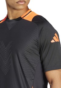Zwart sportshirt met oranje accenten bij de kraag en schouders, voorzien van geometrische patronen en een gestructureerde afwerking.