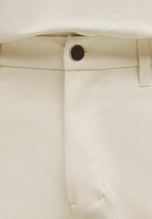 Kalhoty krémové barvy s hladkou texturou, vybavené viditelným zapínacím knoflíkem a čistým designem pasu.