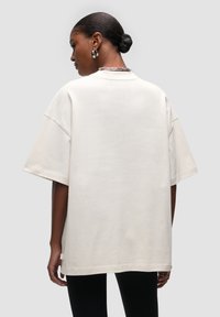 T-shirt oversize in cotone crema con maniche corte, colletto rotondo e orlo dritto. Presenta cuciture minime e un design neutro.