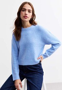 Maglione azzurro chiaro in un tessuto morbido e testurizzato. Presenta un collo rotondo e maniche lunghe, abbinato a jeans in denim scuro.
