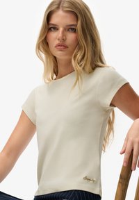 Camiseta de manga corta color crema en una tela elástica con escote redondo y logotipo bordado tonal en el dobladillo.