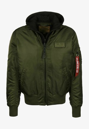 Zielona kurtka bomberka z kapturem, zapinana na zamek z przodu, z ściągaczami przy mankietach i u dołu, oraz czerwoną metką na rękawie z napisem "Zdejmij przed lotem."