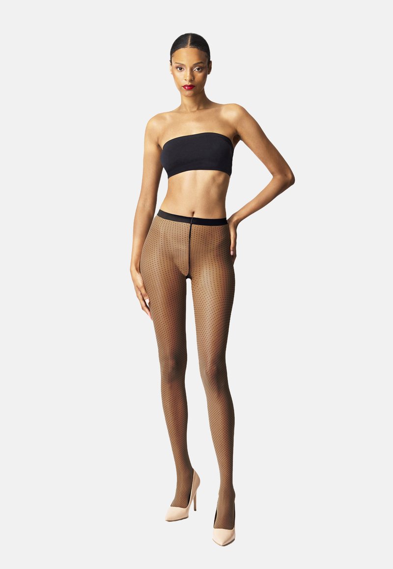 Collant trasparenti color carne in rete con un design a motivo e una vita nera. Abbinati a un top bandeau nero e tacchi color carne.