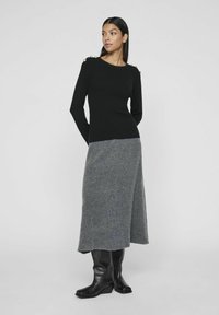 Pull noir avec des accents de boutons dorés sur les épaules, associé à une jupe en mélange de laine grise et à des bottes noires montant jusqu'aux genoux. Textures lisses tout au long.
