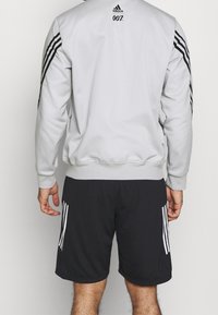 Gray athletic sweatshirt with black stripes, featuring '007' logo on back; paired with black shorts displaying white stripes on side.