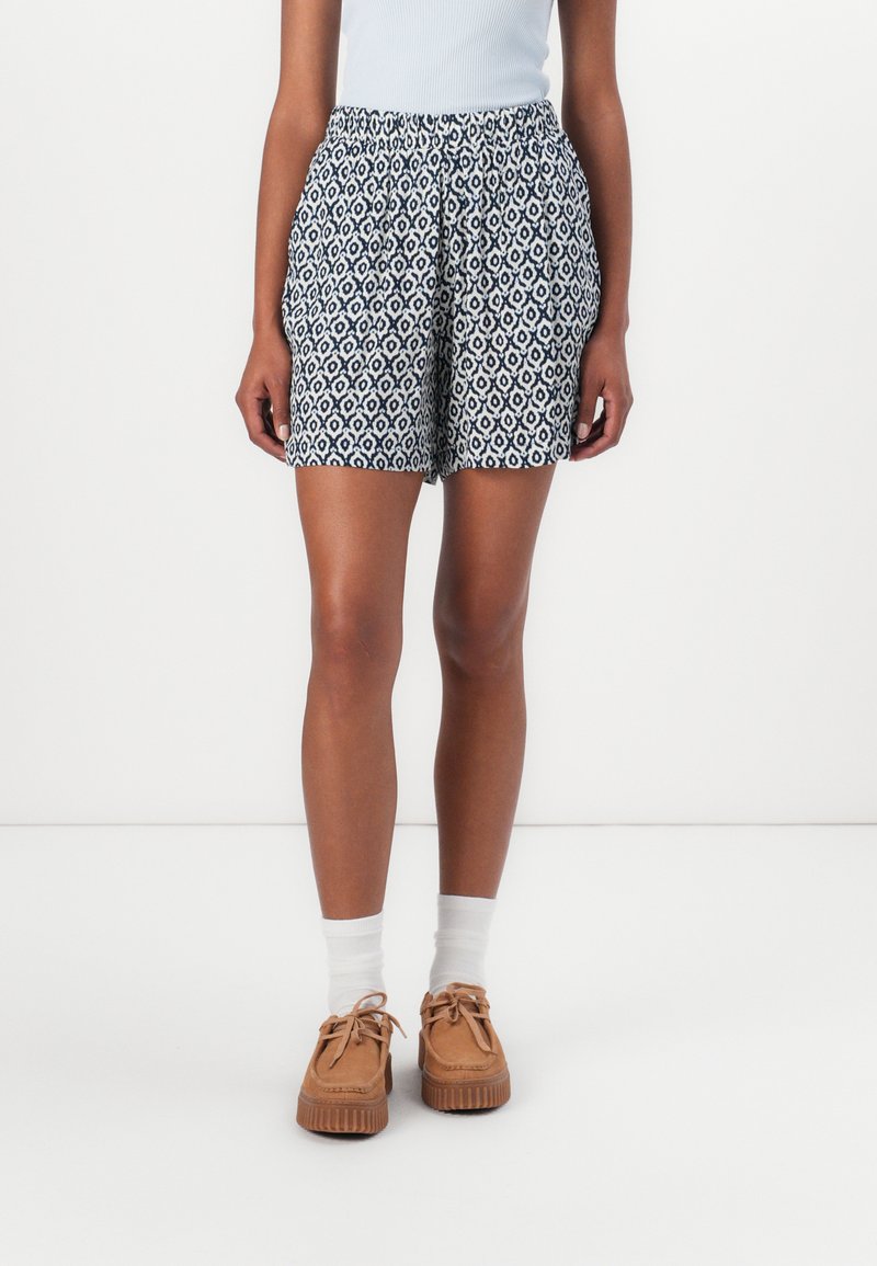 Patterned shorts in navy and white, featuring a drawstring waist. Paired with white socks and tan shoes with a textured sole.