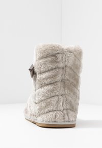 Bottine à cheville en fausse fourrure grise avec un design texturé et matelassé. Dotée d'un petit nœud décoratif et d'une semelle plate de couleur marron clair.