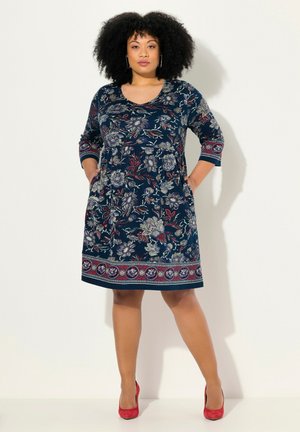 La robe présente un motif floral dans des tons de bleu marine, rouge et gris. Longueur mi-genou avec des manches trois-quarts et des poches. Ourlet uni avec des accents décoratifs.