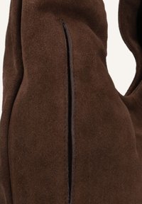 Bruine suede tas met een gladde textuur, zachte afwerking en een verticale sleufdetail. Het ontwerp is eenvoudig zonder zichtbare hardware.