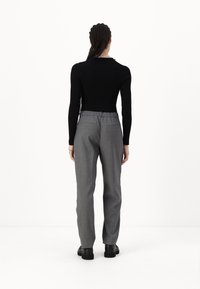 Un haut noir à manches longues côtelé associé à un pantalon gris sur mesure, avec une taille élastique et des poches arrière, porté avec des chaussures plates noires.