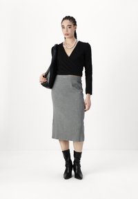 Top negro de tirantes, falda midi de canalé gris y botas negras hasta la rodilla; la modelo sostiene un bolso negro de hombro; fondo neutro.