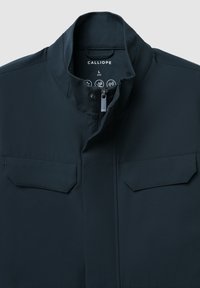 Giacca a zip di colore blu scuro, realizzata in tessuto liscio. Caratterizzata da un colletto alto e due tasche a pattina sul davanti. Etichetta indicante la taglia L.