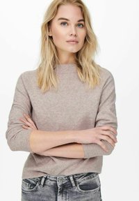 Lichtroze gebreide trui met een ronde hals en lange mouwen, met een gestructureerde afwerking. Gecombineerd met vervaagde grijze jeans.