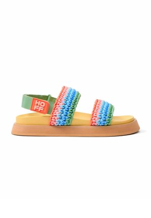 Sandalias multicolores con tiras trenzadas en rosa, azul y verde, una plantilla amarilla y una suela marrón texturizada con una correa verde en el tobillo.