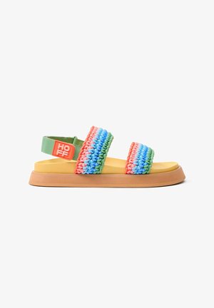 Sandalias multicolores con tiras trenzadas en rosa, azul y verde, una plantilla amarilla y una suela marrón texturizada con una correa verde en el tobillo.