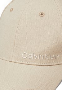 Beige baseballcap van textiel met een gestructureerd oppervlak, voorzien van een gebogen klep en een geborduurd "Calvin Klein" logo in dezelfde kleur.