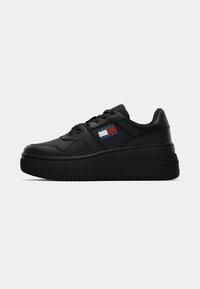 Black leather sneaker with a chunky sole, featuring a logo patch in red, white, and blue, and a rounded toe design. Textured rubber outsole.