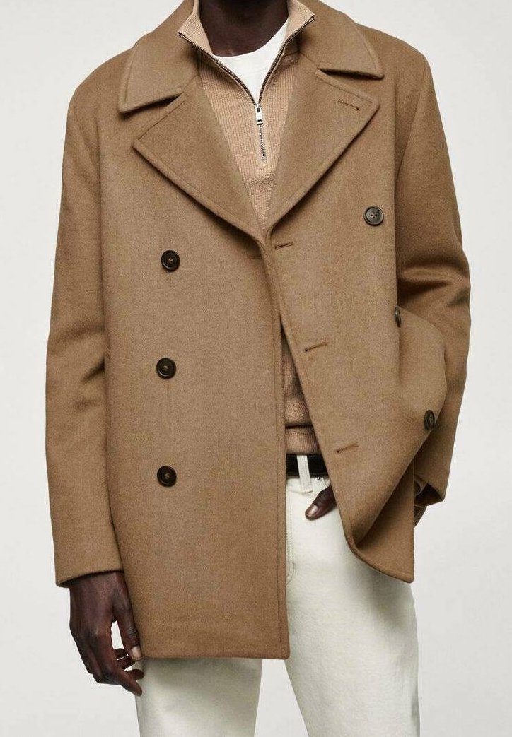 Abrigo de lana beige tipo peacoat con solapas anchas y cierre de botones de doble botonadura. Acentuado con botones oscuros, superpuesto sobre un suéter crema y pantalones claros.