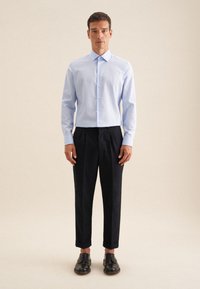 Camicia azzurro chiaro con maniche lunghe, abbinata a pantaloni neri e scarpe nere. La camicia presenta un colletto classico e chiusura con bottoni.