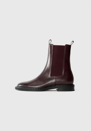 Brown leather Chelsea boot featuring elastic side panels, a pull tab, a rounded toe, and a low block heel, with a smooth texture.
