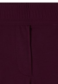 Gros plan d'une ceinture élastique violet foncé sur un pantalon en tissu doux avec des coutures visibles et une couture verticale partielle.