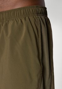 Olive green shorts made of lightweight fabric with an elastic waistband and side mesh pockets. Includes a smooth texture and neat stitching.