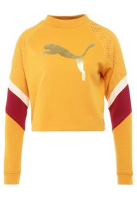 Żółta skrócona bluza z siateczkowymi detalami na ramionach, długimi rękawami, golfem i złotym logo Pumy z przodu. Czerwone i białe akcenty.