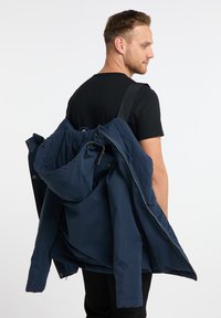 Tamsiai mėlyna išorinė striukė su gobtuvu, pagaminta iš lygios medžiagos, uždengta fliso vidine striuke. Yra reguliuojamos raišteliai ir užtrauktukai.