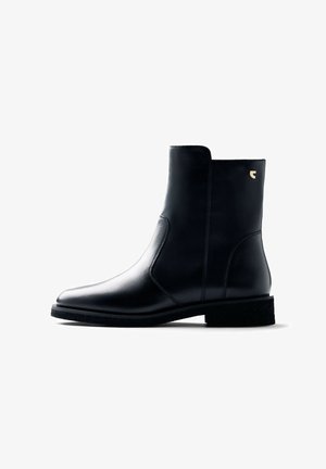 Bottine en cuir noir avec une finition lisse, bout rond et tige courte. Comprend un panneau élastique sur le côté et une semelle texturée avec un accent logo doré.