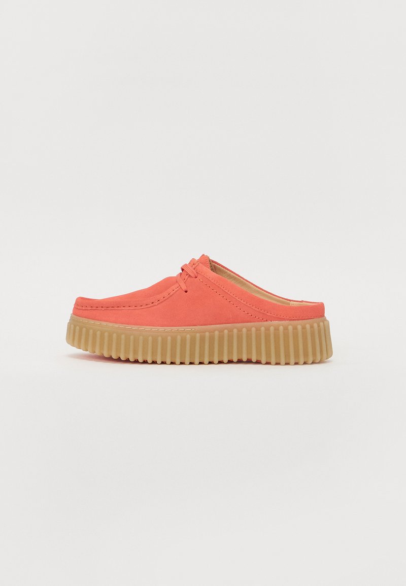Chaussons en suède corail avec un bout arrondi, dotés d'une semelle en caoutchouc beige texturé avec des stries et de coutures décoratives sur la tige.
