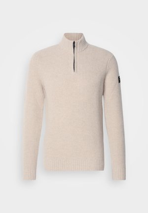 Suéter beige con cremallera en el cuello y textura acanalada, de mangas largas y puños elásticos. Presenta una cremallera en contraste y un parche de logo en el lateral.