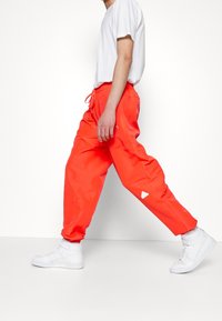 Person som går och bär ljusoranga byxor, en vit t-shirt och vita högskridskor mot en helt vit bakgrund.