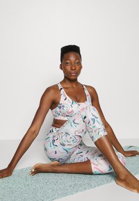 Conjunto de roupa desportiva estampada, composto por um soutien desportivo e leggings 3/4 em tons pastéis com desenhos florais abstratos e um ajuste justo.