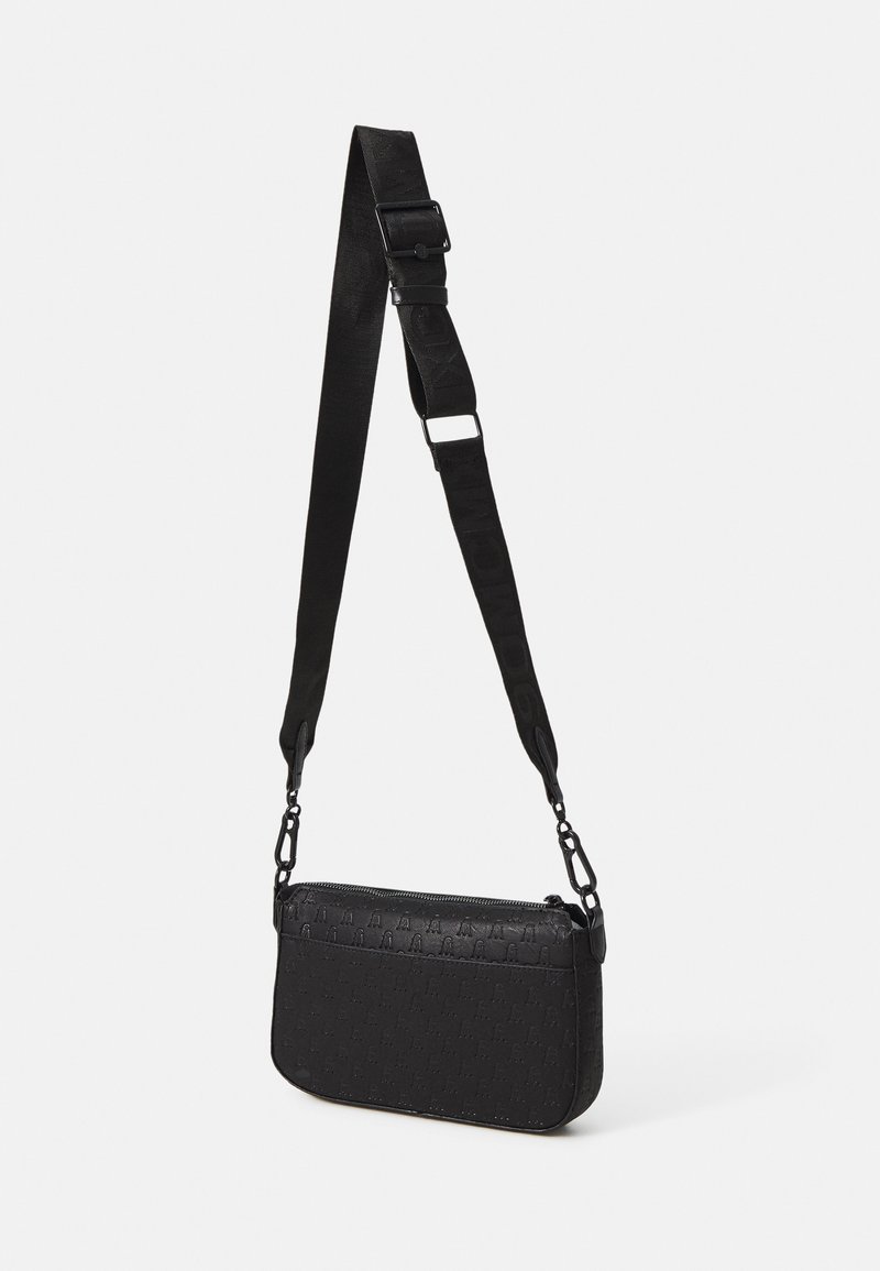 Sac bandoulière noir avec une sangle large ajustable et un motif en relief, suspendu sur un fond clair uni.