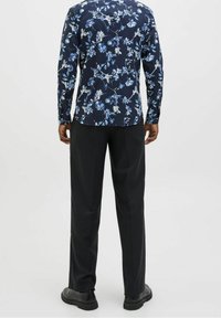 Camicia a stampa floreale in blu navy con fiori blu e bianchi, abbinata a pantaloni neri. Caratterizzata da maniche lunghe e colletto standard.