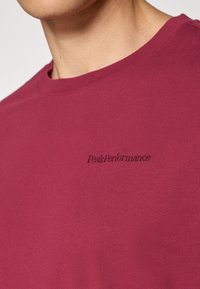 Close-up of a person wearing a maroon crewneck shirt with "Peak Performance" embroidered on the chest.
