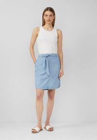 Lichtblauwe denimbroekrok met een gestrikte taille, twee zijzakken en een gladde textuur. Gecombineerd met een aansluitend wit tanktop en sandalen.
