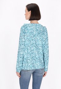 Cămașă ușoară cu glugă, în carouri florale albastre, cu mâneci lungi. Prezintă o croială lejeră și detalii cu cusătură pe partea din spate.