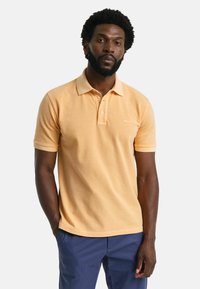 Ljusorange polo skjorta med krage, två-knappsknäppning och broderad logotyp. Korta ärmar och en strukturerad tyg.