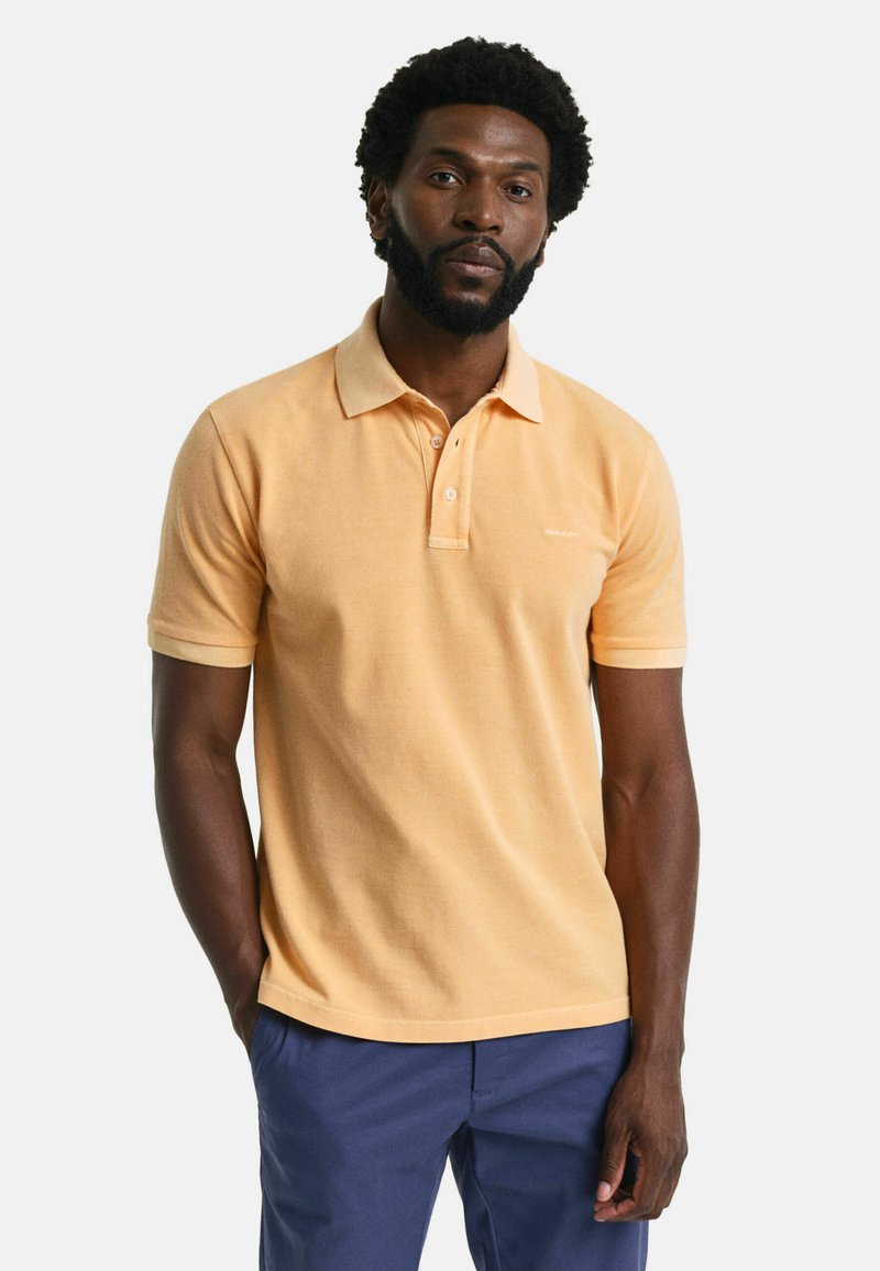 Ljusorange polo skjorta med krage, två-knappsknäppning och broderad logotyp. Korta ärmar och en strukturerad tyg.