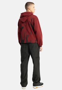 Czerwono-czarna bluza z kapturem w stylu tie-dye z przednią kieszenią kangurką, zestawiona z czarnymi spodniami cargo z bocznymi kieszeniami i teksturowanym materiałem.