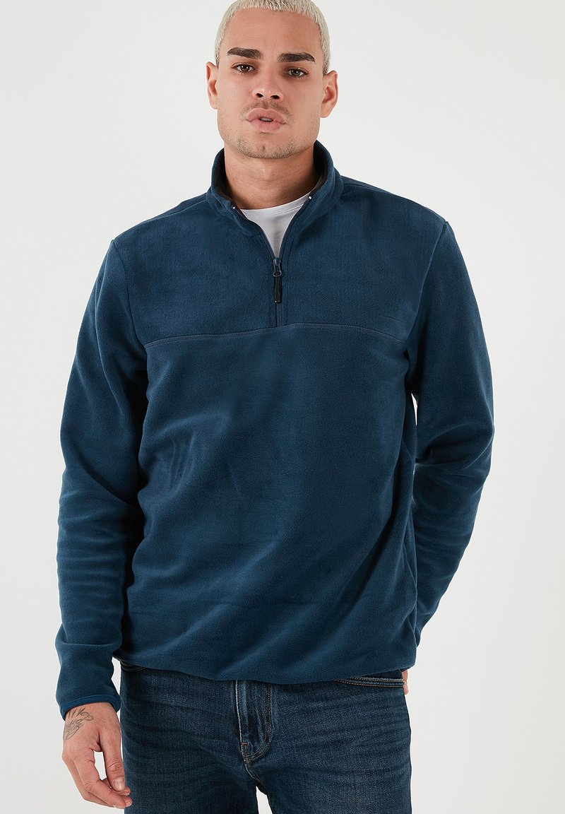 Pullover in pile blu navy con collo a mezza zip, maniche lunghe e una texture liscia. Presenta un leggero pannello a contrasto sul petto.