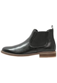 Stivale alla caviglia in pelle nera con finitura testurizzata, pannelli laterali elasticizzati e tacco in legno marrone. Presenta una linguetta per una facile calzata.