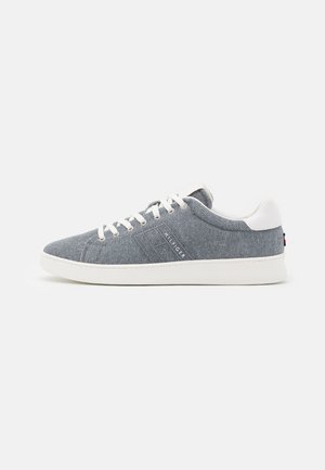 Niedrig geschnittener grauer Stoff-Sneaker mit weißen Schnürsenkeln und Sohle, weißer Fersenlasche und "Hilfiger"-Branding an der Seite.