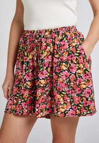 Shorts fleuris avec une taille élastique, présentant des fleurs roses, orange et vertes éclatantes sur un fond noir ; comprend des poches.