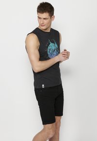 Svart ärmlös T-shirt med grafiskt tryck i blått och turkost, tillsammans med svarta denimshorts. Slät tyg och figurnära design.