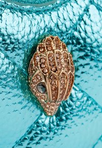 Borsa turchese con finitura metallica testurizzata, caratterizzata da una chiusura dorata decorata con gemme trasparenti e nere in un design dettagliato.