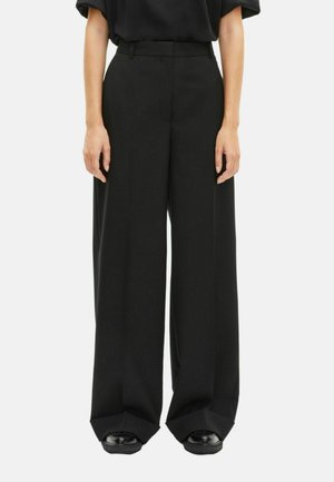 Pantalons larges noirs à taille haute, avec une texture lisse et des lignes épurées. Le tissu tombe en drapé lâche jusqu'aux chevilles, améliorant le confort.