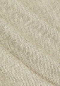 Jasnoszara tkanina o teksturowanym, plecionym wzorze, charakteryzująca się miękką i nieco puszystą powierzchnią. Materiał układa się w delikatne fałdy.